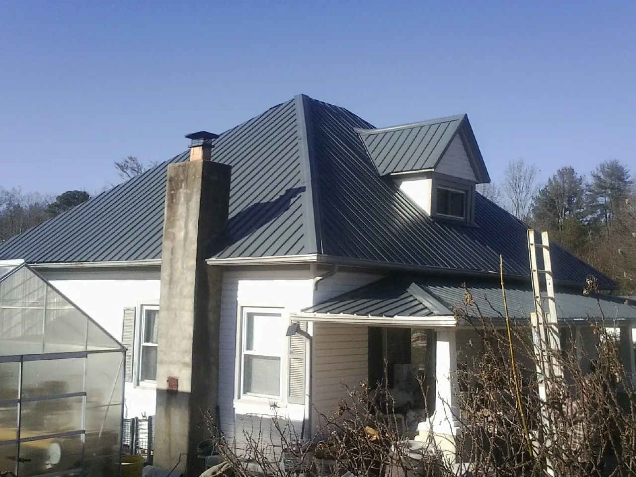 Dark blue standing seam metal roof on a white farmhouse with dormer — Slate & Tile Roof Repair by Roofing Brothers in Judith Gap