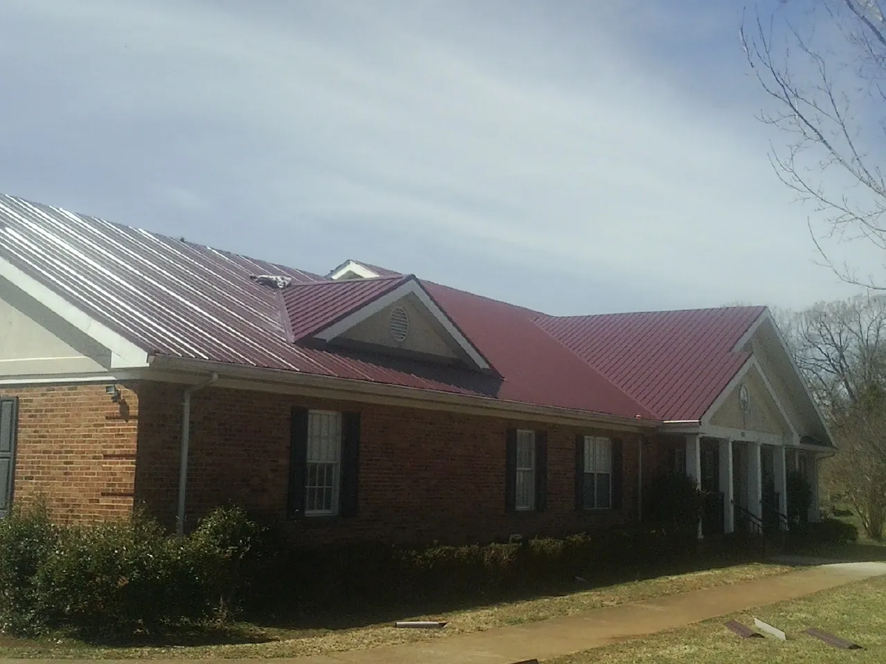 Red metal roof with gabled entries on a long brick building, from a Hail Damage Roof Repair job in Judith Gap
