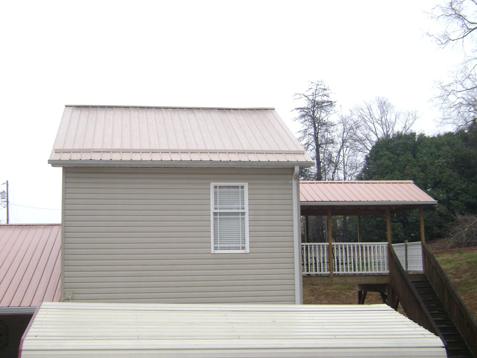 Tan metal roofs on a two story addition and attached porch, from a Roof Replacement job in Judith Gap